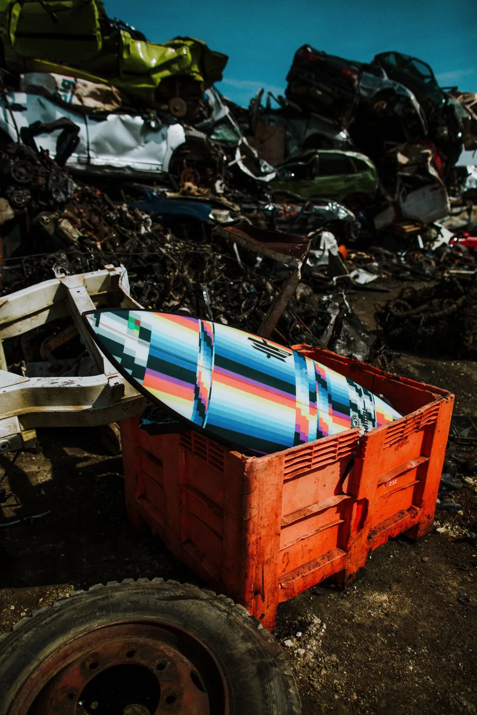 Planche de surf multicolore posée dans une benne orange au milieu de carcasses